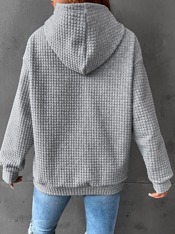 Vue de dos d'une femme portant un sweat à capuche gris clair à texture gaufrée. Ce vêtement ample et décontracté possède des manches longues et un ourlet côtelé. Son tissu épais et doux offre une sensation de confort et de chaleur, idéale pour l'hiver. Le fond gris met en valeur la texture du tissu et le style moderne du sweat à capuche.