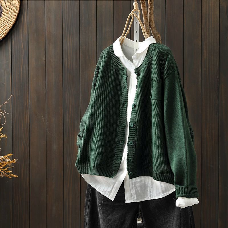 Cardigan oversize pour femme de couleur vert foncé, exposé sur un cintre au-dessus d’une chemise blanche ample. Le modèle présente une maille texturée, une coupe large et des boutons frontaux, offrant un style moderne et décontracté.