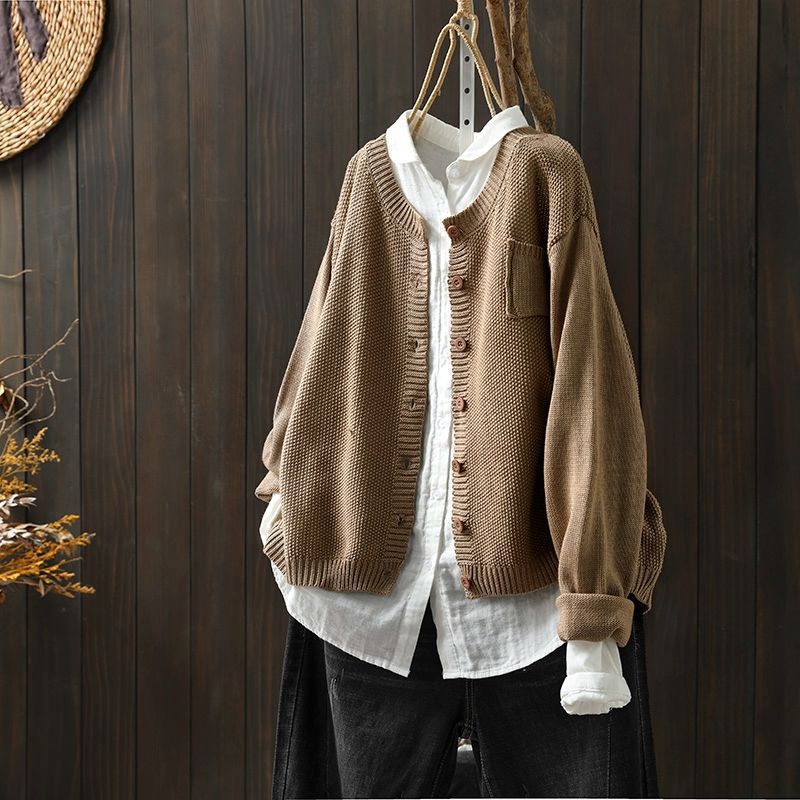 Un cardigan oversize kaki pour femme, suspendu à un cintre par-dessus une chemise blanche ample. Ce cardigan en maille texturée, orné de boutons assortis et d'une coupe décontractée, offre un style moderne, naturel et casual.