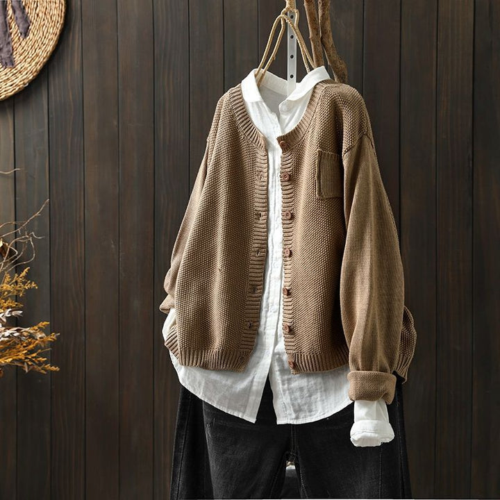 Un cardigan oversize kaki pour femme, suspendu à un cintre par-dessus une chemise blanche ample. Ce cardigan en maille texturée, orné de boutons assortis et d'une coupe décontractée, offre un style moderne, naturel et casual.