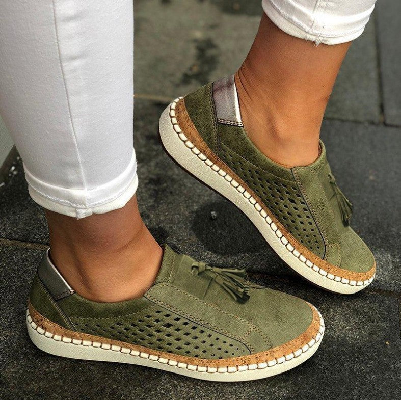 pantoufles plates vert kaki en suédine perforée avec pampilles, semelle épaisse blanche et liseré effet liège, portées avec un pantalon blanc.
