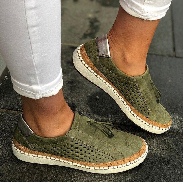 pantoufles plates vert kaki en suédine perforée avec pampilles, semelle épaisse blanche et liseré effet liège, portées avec un pantalon blanc.