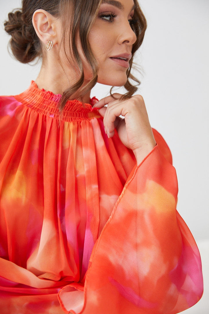 Zoom sur le haut de la robe mini d'été à manches longues pour femme, avec un dégradé de couleurs orange et rose. Le modèle met en valeur le col smocké et les manches évasées, apportant une touche élégante et fluide à la silhouette. Des détails soignés, parfaits pour un look moderne et estival.