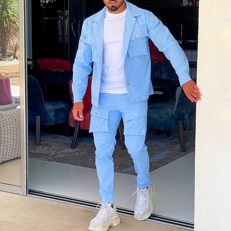 Homme portant un ensemble cargo élégant de couleur bleue claire, composé d’une veste à poches et d’un pantalon assorti. Il marche à l’intérieur d’une maison moderne, avec un fond de décor stylé comprenant une table et des fauteuils. Il porte un t-shirt blanc et des baskets modernes, créant un look décontracté et élégant.
