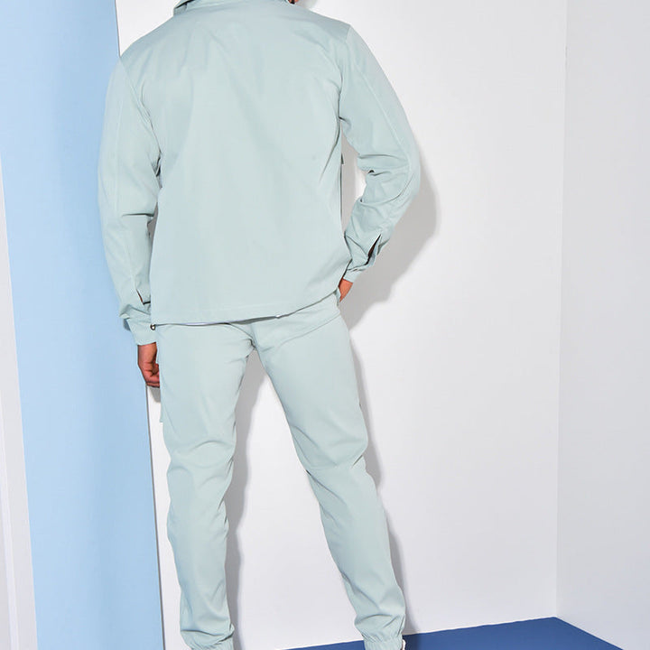 Homme portant un ensemble élégant de couleur bleu pâle avec une chemise et un pantalon cargo. Le modèle est vu de dos dans un cadre minimaliste avec des murs aux couleurs pastel, mettant en valeur le style moderne et décontracté de l'ensemble. Le look est à la fois pratique et tendance, idéal pour un style urbain.