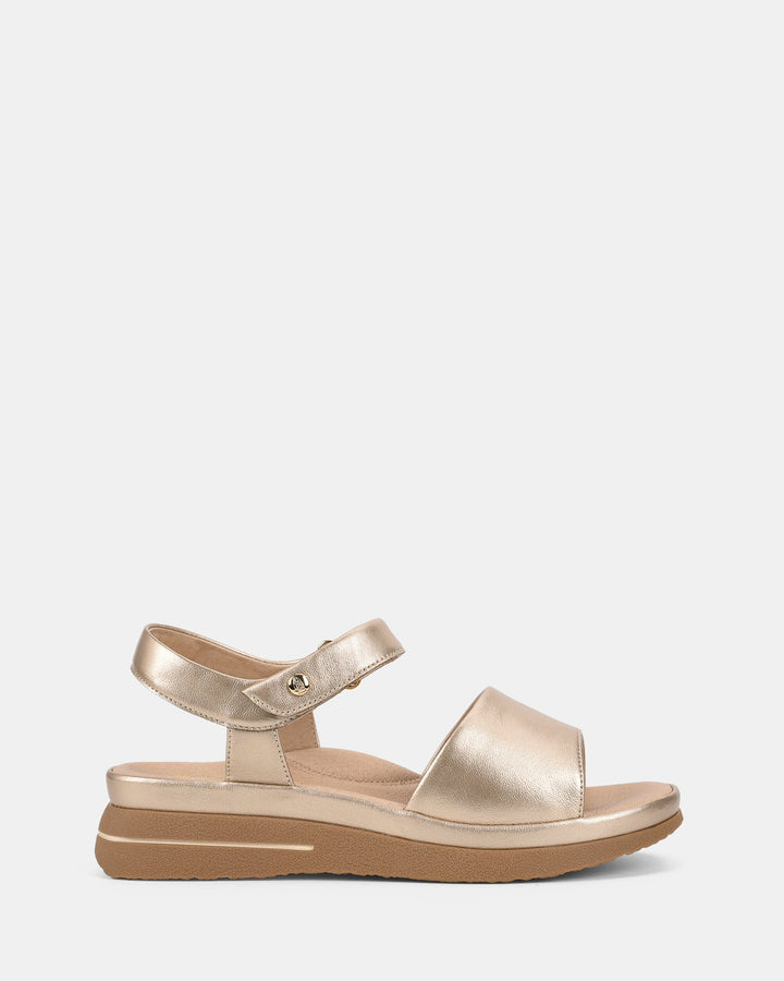 Vue latérale des sandales pour femmes au fini métallisé doré, avec bride avant large et sangle de cheville ajustable. Semelle épaisse offrant confort et style pour un look moderne et estival.