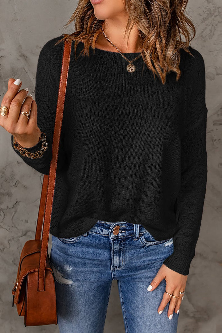 Une femme portant un pull décontracté à coupe ample, associé à un jean déchiré. Elle accessoirise avec un sac en cuir en bandoulière et des bijoux superposés, dégageant un look stylé et décontracté.