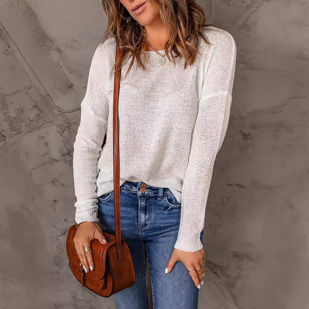 Une femme portant un pull décontracté à coupe ample, associé à un jean déchiré. Elle accessoirise avec un sac en cuir en bandoulière et des bijoux superposés, mettant en valeur un look chic et sans effort.
