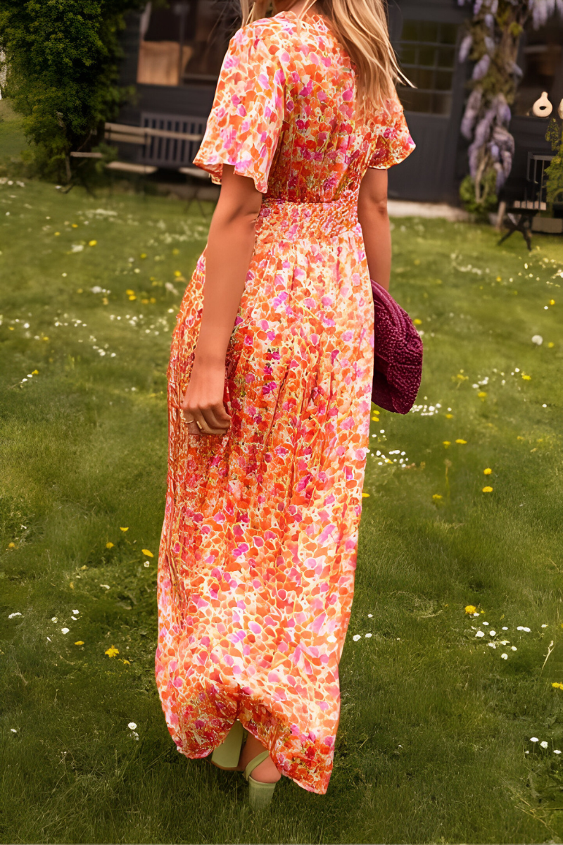 Vue arrière de la robe longue à col en V pour femme, modèle tendance. Cette robe fluide aux couleurs vives et aux motifs floraux se distingue par son dos élastiqué qui met en valeur la silhouette. Portez-la avec des accessoires modernes, comme un sac en crochet violet et des sandales à talons, pour un look à la fois élégant et décontracté.