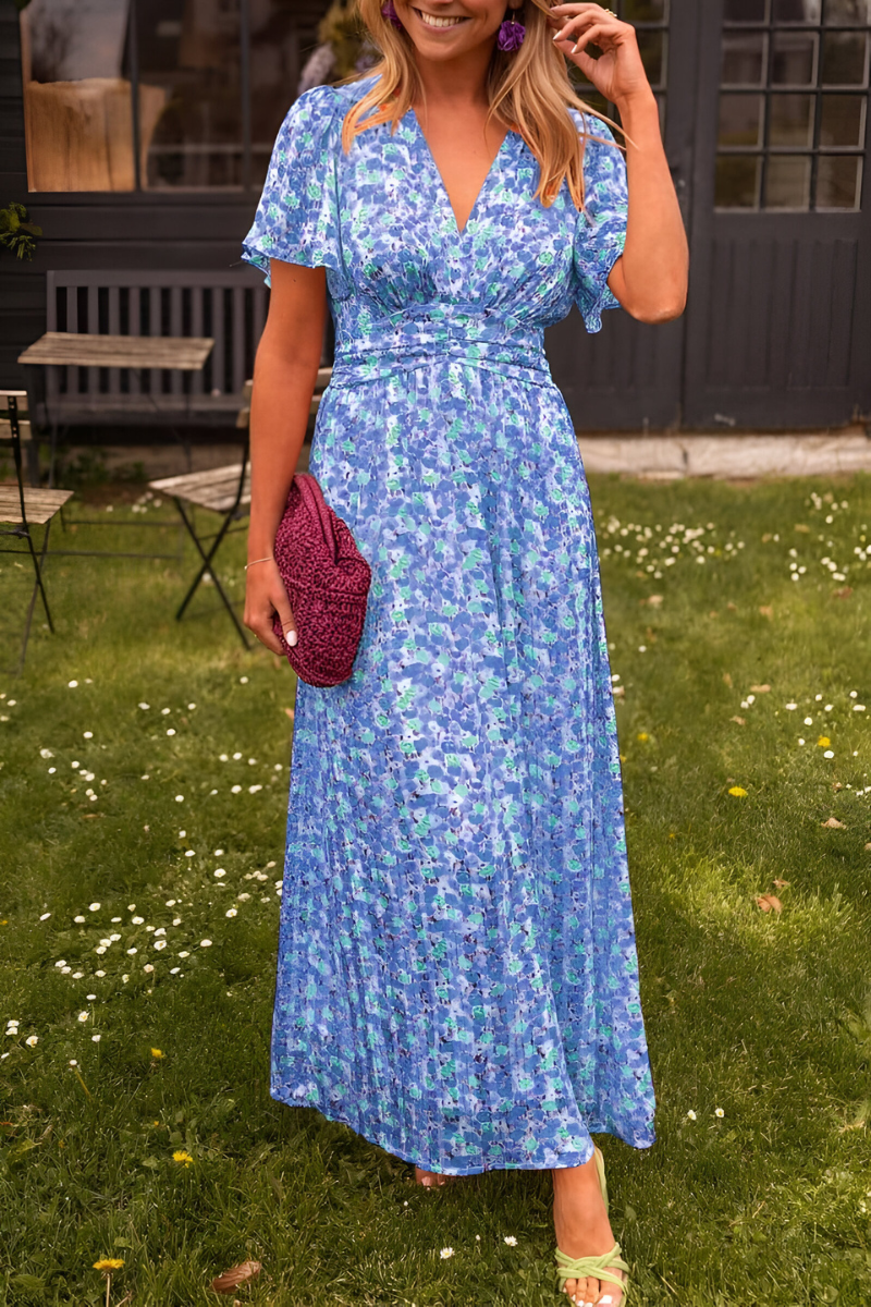 Robe longue à col en V pour femme, modèle tendance. Cette robe fluide présente un motif floral délicat aux nuances de bleu et de vert, idéale pour les journées ensoleillées. Elle est associée à un sac en crochet violet et des sandales assorties, offrant une allure élégante et décontractée, parfaite pour vos sorties estivales.