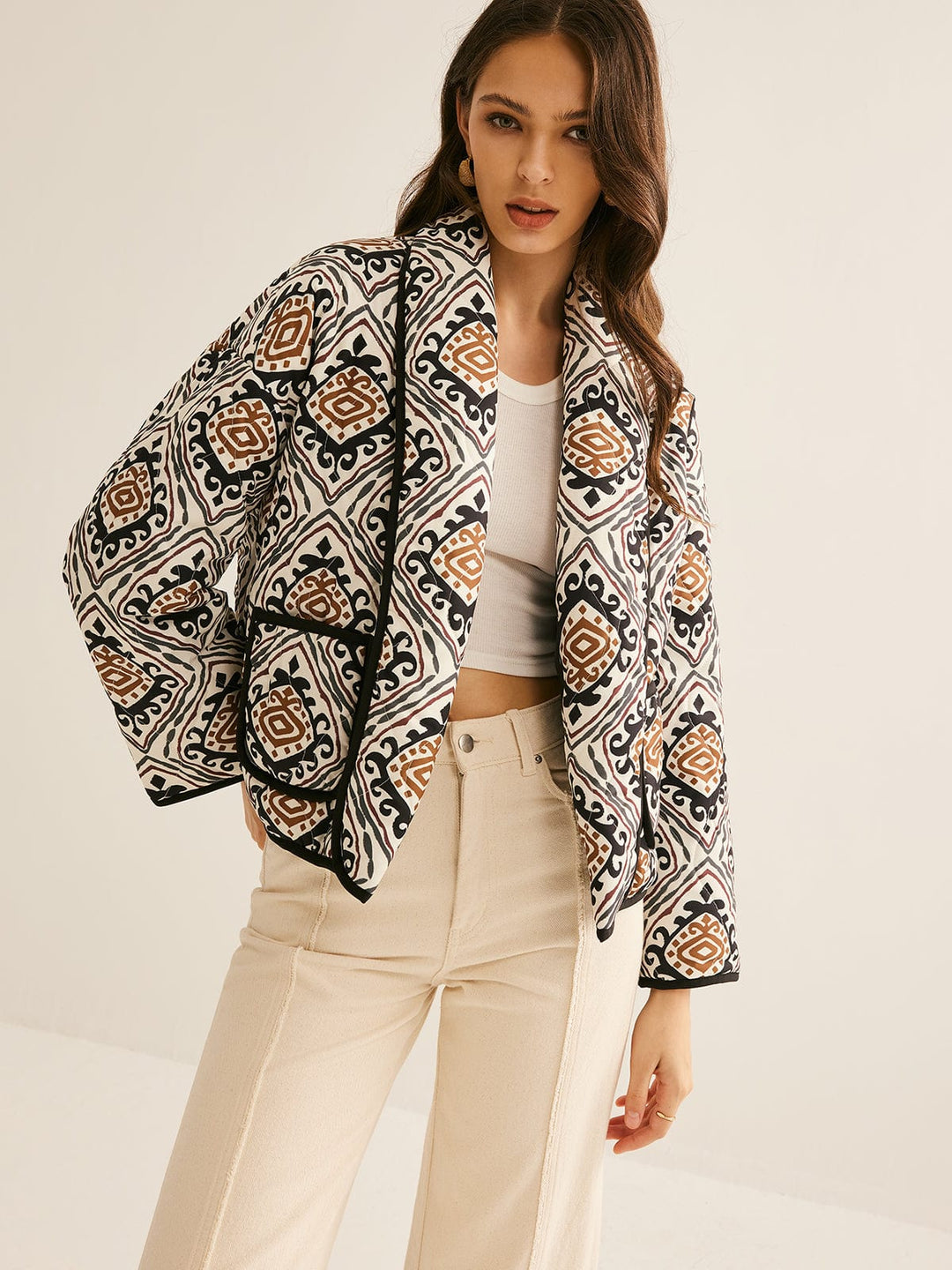 veste ample imprimée de motifs géométriques noirs, blancs et bruns, manches larges, bordure noire et fermeture ouverte, portée avec un haut clair et un pantalon clair dans un cadre neutre, style moderne.