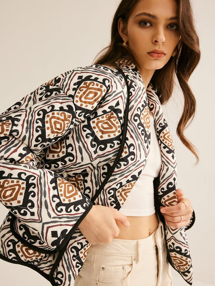 veste ample imprimée de motifs géométriques noir, blanc et brun, manches longues et bordure noire, portée ouverte sur un top clair et un pantalon clair dans un cadre neutre, style moderne.