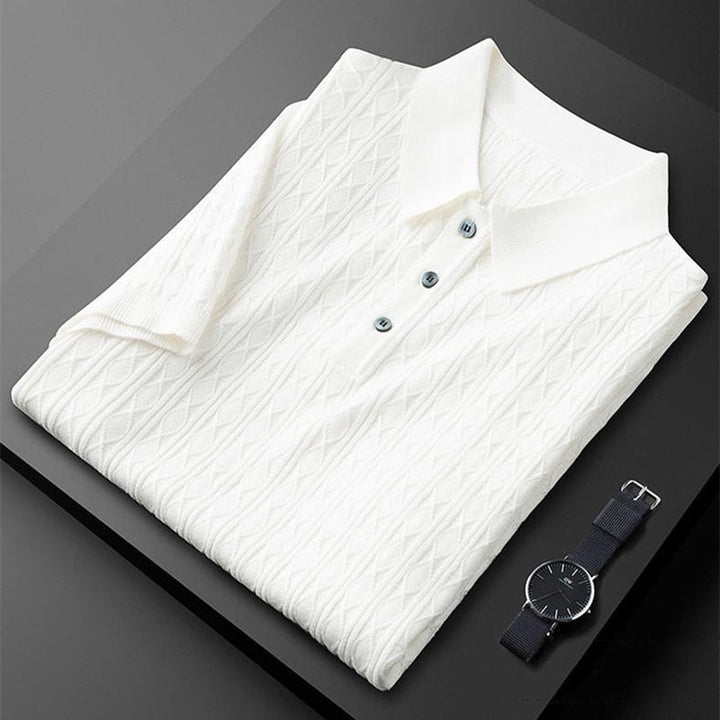 Polo premium pour homme Sabin, couleur blanc cassé, plié avec soin, doté d’un col classique et de boutons élégants, présentant une texture raffinée et tendance, accompagné d’une montre moderne pour un style chic et sophistiqué.