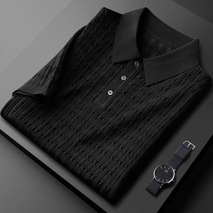 Polo premium pour homme Sabin, noir élégant avec texture en maille raffinée, plié avec soin, doté d’un col classique et de boutons discrets, présenté avec une montre moderne pour un look tendance et sophistiqué.