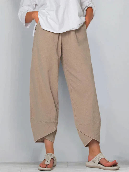 Pantalon droit pour femme de couleur beige, coupe ample et fluide, taille haute avec plis discrets, longueur cheville, porté avec une chemise blanche et des sandales plates, vue de face du buste jusqu’aux pieds sur fond clair.