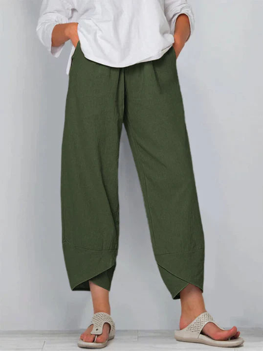 Pantalon droit pour femme de couleur vert olive, coupe ample et fluide, taille haute avec plis discrets, longueur cheville avec ourlets croisés, porté avec une chemise blanche et des sandales plates, vue de face du buste jusqu’aux pieds sur fond clair.