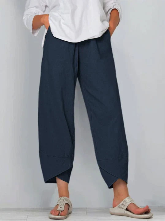 Pantalon droit pour femme de couleur bleu marine, coupe ample et fluide, taille haute avec plis discrets, longueur cheville avec ourlets croisés, porté avec une chemise blanche et des sandales plates, vue de face du buste jusqu’aux pieds sur fond clair.