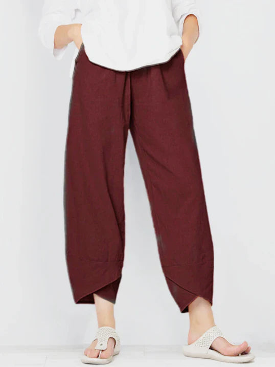 Pantalon droit pour femme de couleur bordeaux, coupe ample et fluide, taille haute avec plis discrets, longueur cheville avec ourlets croisés, porté avec une chemise blanche et des sandales plates, vue de face du buste jusqu’aux pieds sur fond clair.