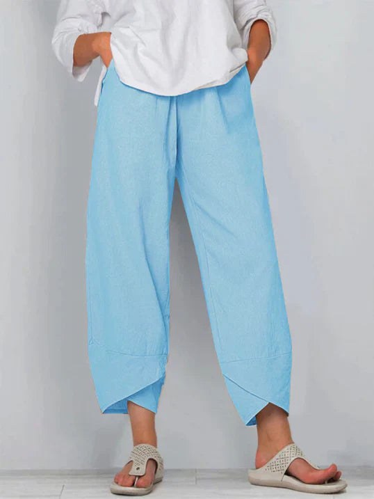 Pantalon droit pour femme de couleur bleu clair, coupe ample et fluide, taille haute avec plis discrets, longueur cheville avec ourlets croisés, porté avec une chemise blanche et des sandales plates, vue de face du buste jusqu’aux pieds sur fond clair.
