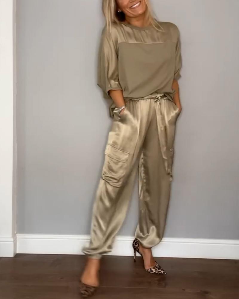 Femme portant un ensemble élégant composé d'un haut fluide beige et d'un pantalon cargo satiné avec des poches latérales. Elle porte des escarpins léopard, créant un look à la fois sophistiqué et décontracté.