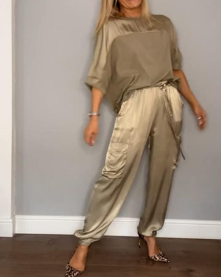 Femme portant un ensemble chic avec un haut fluide beige et un pantalon cargo satiné, orné de poches latérales. Elle porte des escarpins léopard, créant un look élégant et raffiné.