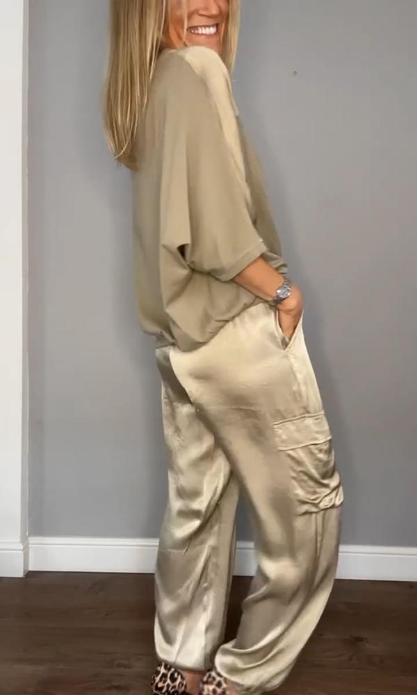 Femme souriante portant un ensemble élégant composé d'un haut fluide beige et d'un pantalon cargo satiné avec des poches latérales. Elle porte des escarpins léopard et un bracelet, créant un look à la fois chic et décontracté.