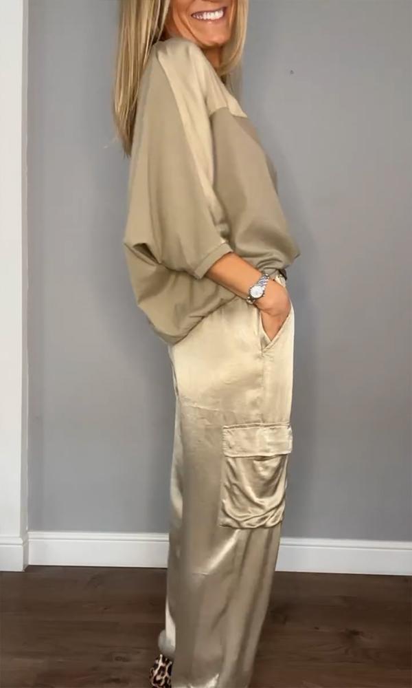 Femme portant un ensemble élégant composé d'un haut fluide beige et d'un pantalon cargo satiné avec des poches latérales. Elle porte des escarpins léopard et un bracelet, créant un look sophistiqué et décontracté, tout en souriant.