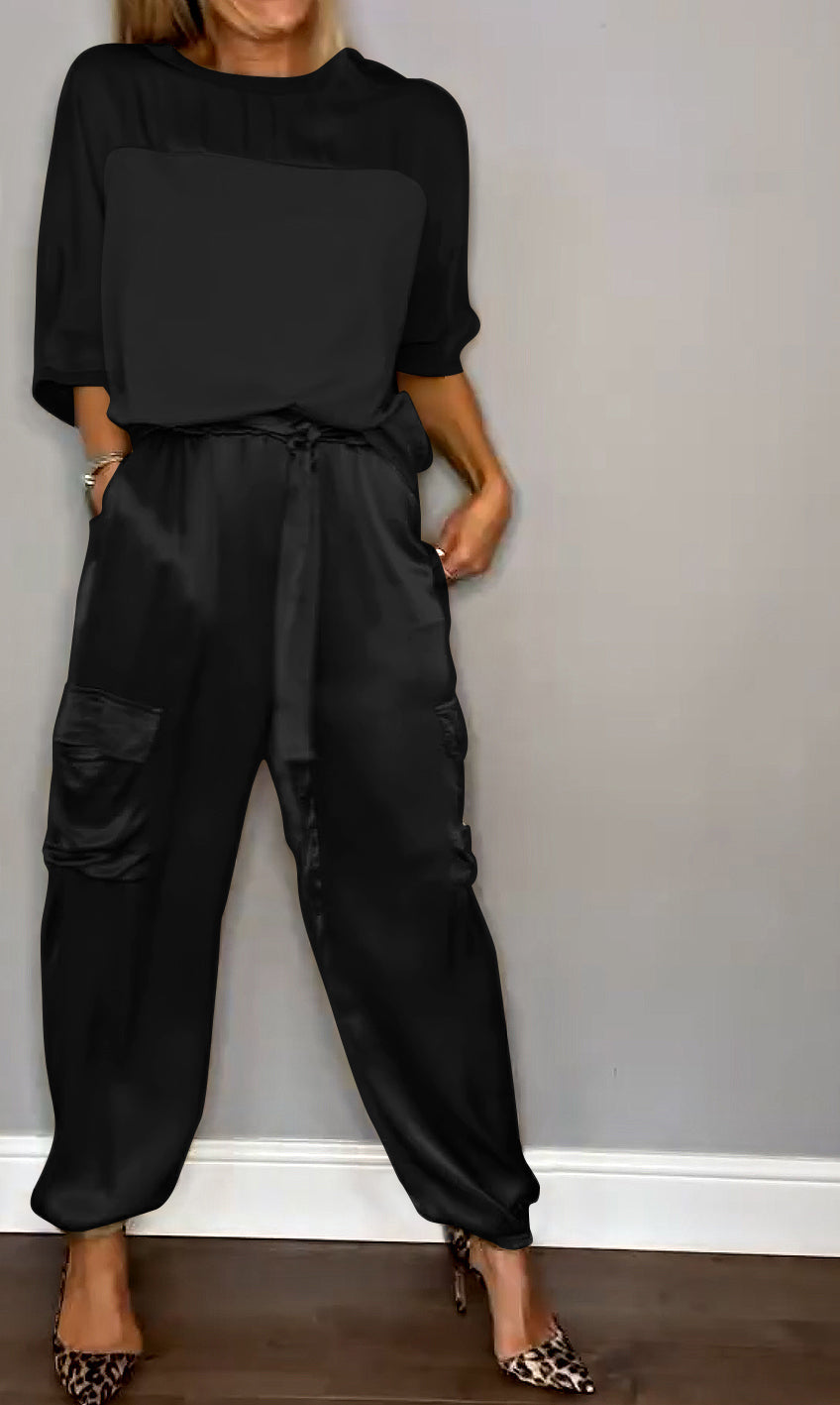 Femme portant un ensemble élégant noir, composé d'un haut fluide et d'un pantalon cargo satiné avec des poches latérales. Elle porte des escarpins léopard, créant un look à la fois chic et sophistiqué.