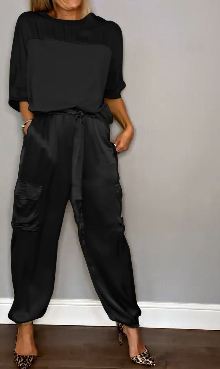 Femme portant un ensemble élégant noir, composé d'un haut fluide et d'un pantalon cargo satiné avec des poches latérales. Elle porte des escarpins léopard, créant un look à la fois chic et sophistiqué.