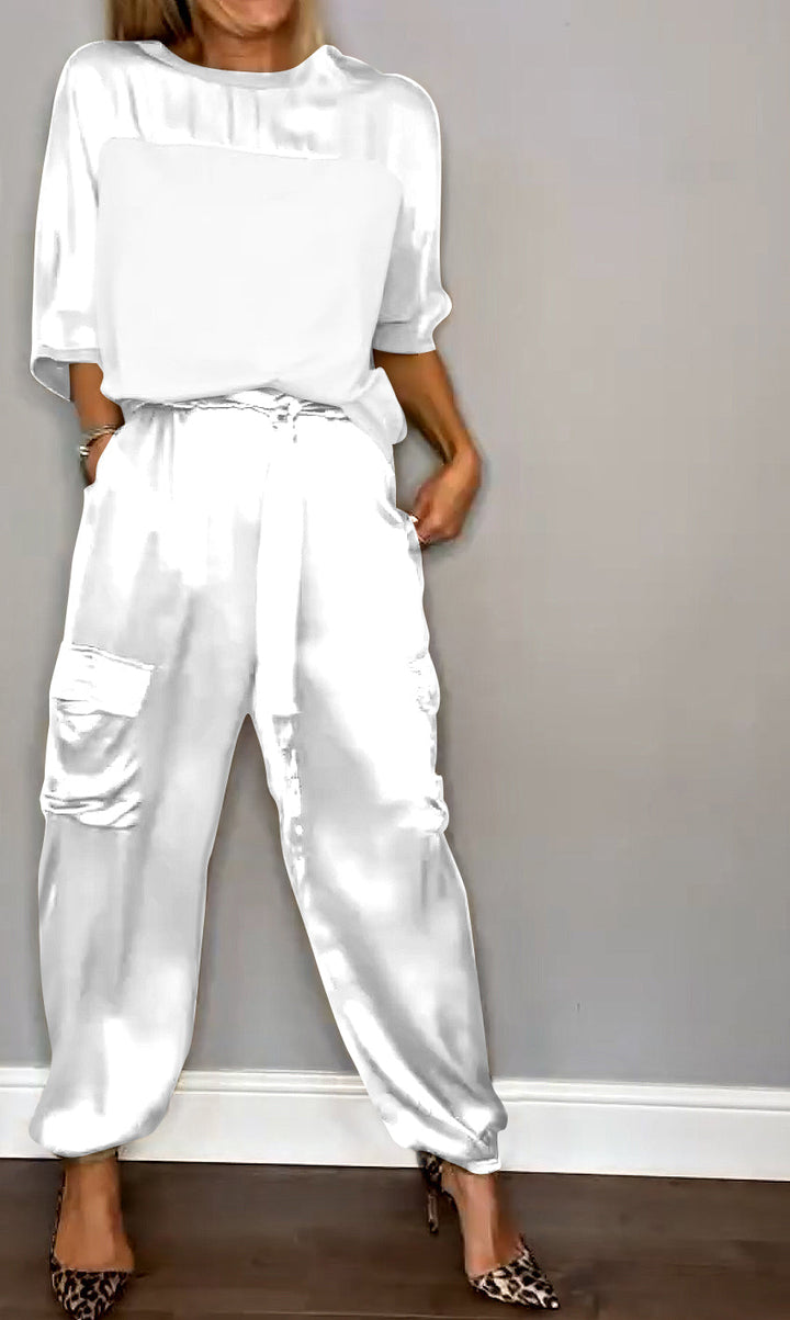 Femme portant un ensemble élégant blanc, composé d'un haut fluide et d'un pantalon cargo satiné avec des poches latérales. Elle porte des escarpins léopard, créant un look à la fois chic et sophistiqué.