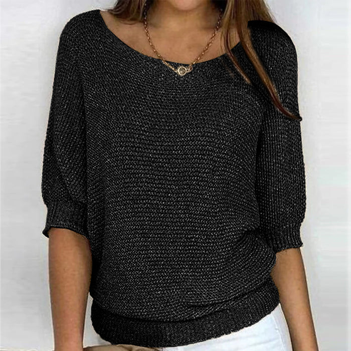 Une femme porte un haut tricoté noir élégant à manches 3/4 et à coupe décontractée. Le haut présente un col en U et est associé à un pantalon blanc, complété par un collier en chaîne délicat, donnant à l'ensemble un look chic et décontracté.