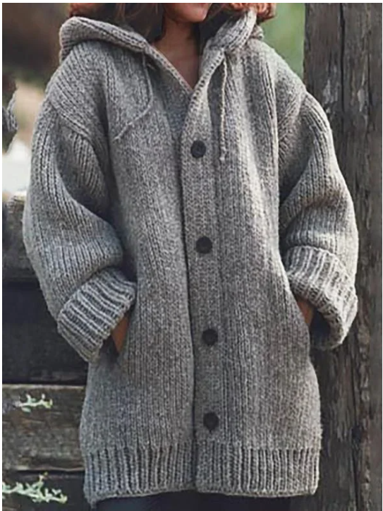 Femme portant un long cardigan gris chiné en grosse maille, à manches larges, poches latérales et gros boutons foncés, offrant un style hivernal chaud et décontracté.