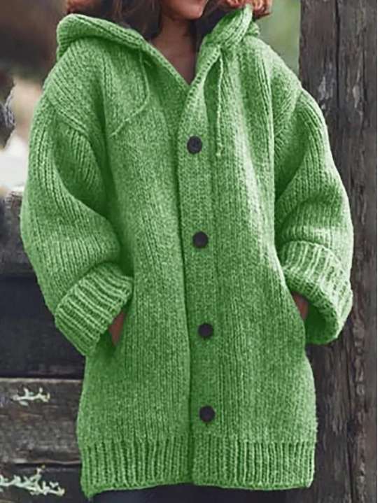 Femme portant un long cardigan vert vif en grosse maille, à manches larges, poches latérales et gros boutons foncés, offrant un style hivernal chaud et décontracté.