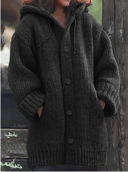 Femme portant un long cardigan noir en grosse maille, à manches larges, poches latérales et gros boutons foncés, offrant un style hivernal chaud et décontracté.