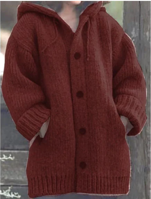 Femme portant un long cardigan rouge brique en grosse maille, à manches larges, poches latérales et gros boutons ton sur ton, offrant un style hivernal confortable et chaud.