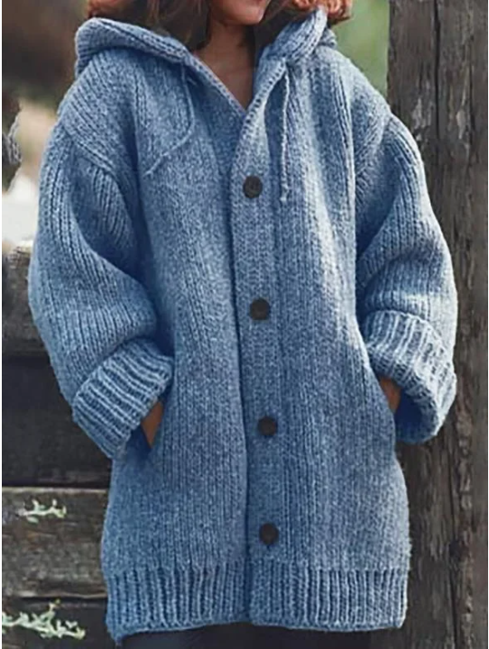 Femme portant un long cardigan bleu ciel en grosse maille, à manches larges, poches latérales et gros boutons foncés, offrant un style hivernal chaud et décontracté.