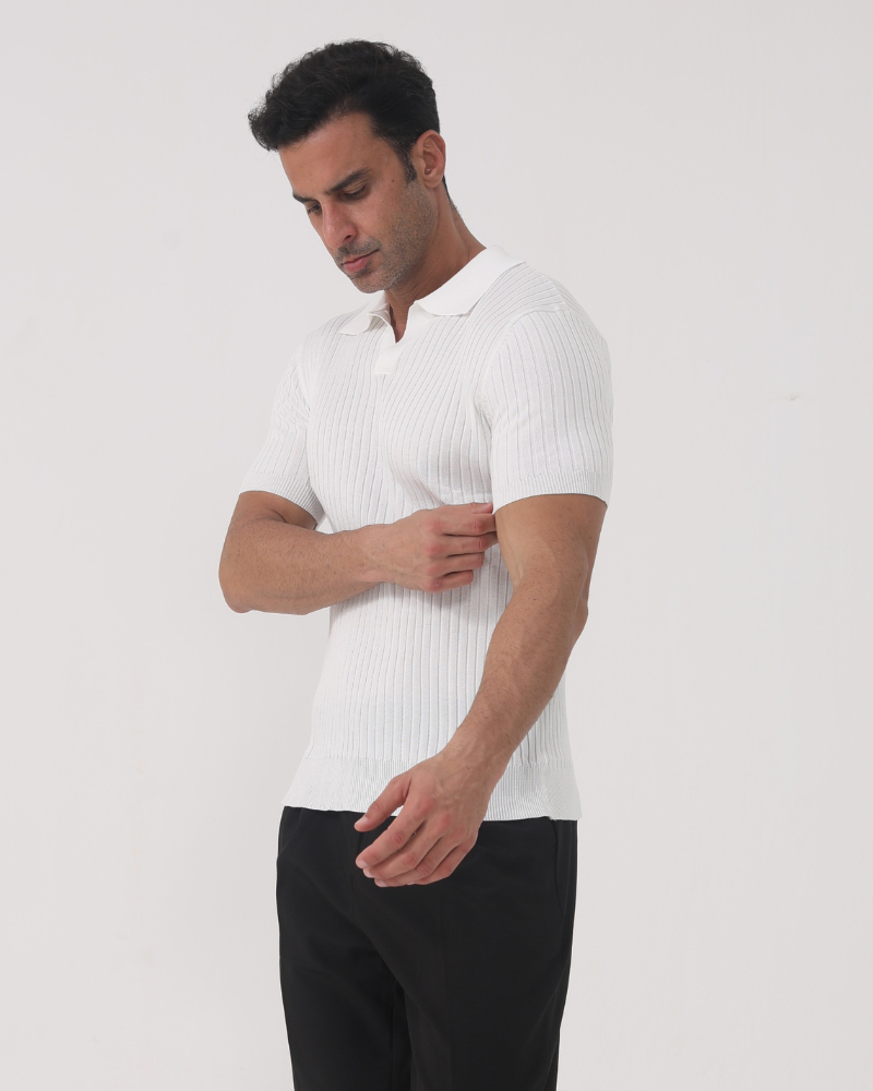 Homme portant le polo Sully en maille côtelée blanc, à manches courtes avec col en V, ajustant la manche, mettant en valeur la coupe près du corps et le style moderne et tendance, associé à un pantalon sombre.