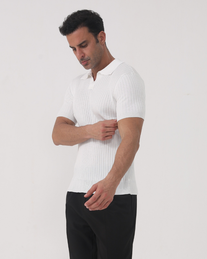 Homme portant le polo Sully en maille côtelée blanc, à manches courtes avec col en V, ajustant la manche, mettant en valeur la coupe près du corps et le style moderne et tendance, associé à un pantalon sombre.