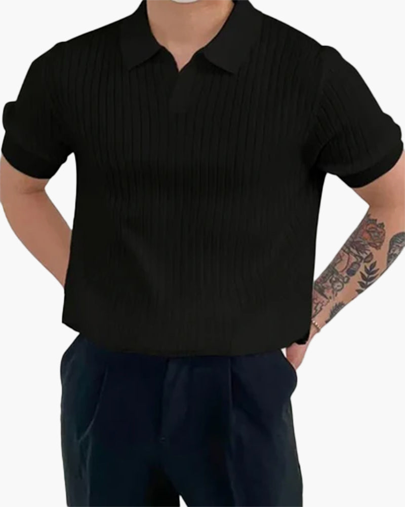 Homme portant le polo Sully en maille côtelée noir, à manches courtes avec col en V, offrant une texture élégante et un style moderne et tendance, associé à un pantalon sombre.