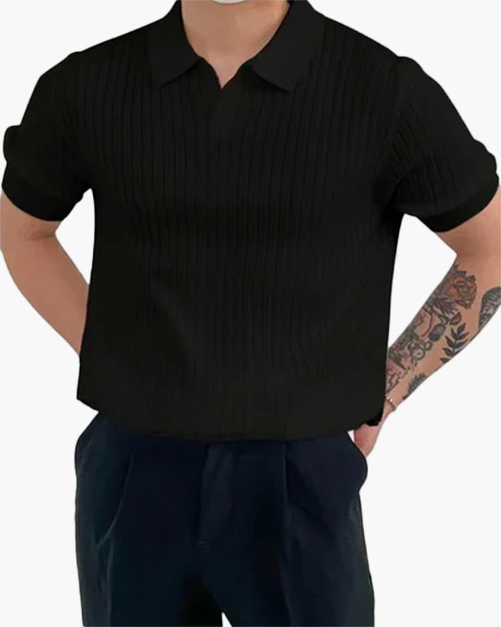 Homme portant le polo Sully en maille côtelée noir, à manches courtes avec col en V, offrant une texture élégante et un style moderne et tendance, associé à un pantalon sombre.
