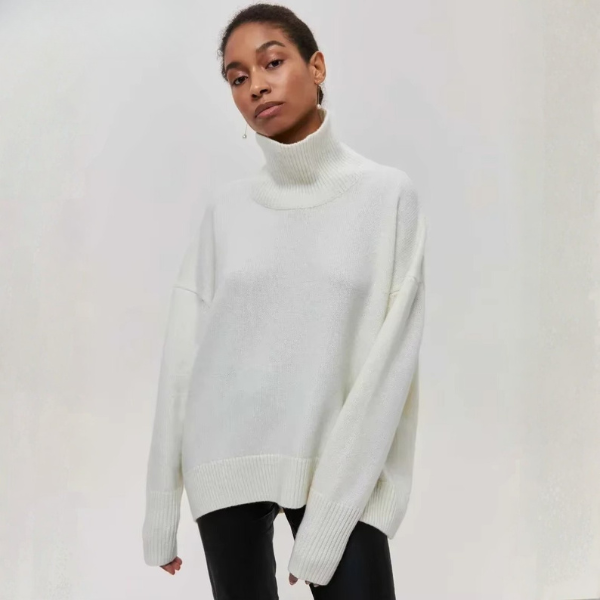Pull oversize à col roulé pour femme, de couleur blanche, avec des manches longues et un ajustement ample. Le pull présente une coupe moderne et décontractée, parfait pour un look élégant et confortable. Il est porté avec un bas noir, créant un contraste subtil et stylé.