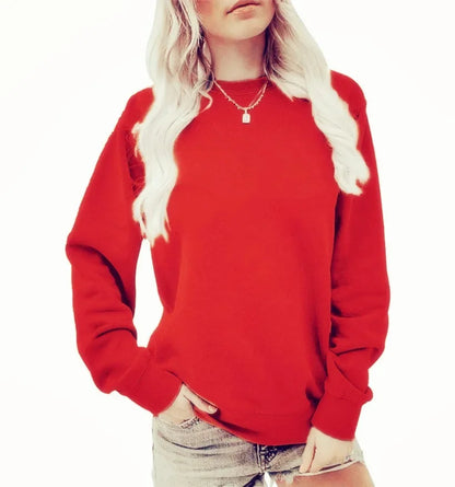 Femme portant un sweat-shirt rouge vif à manches longues, avec un col rond. Elle a des cheveux blonds et porte un collier délicat, associant le sweat avec un short en jean. Elle pose une main sur sa taille.