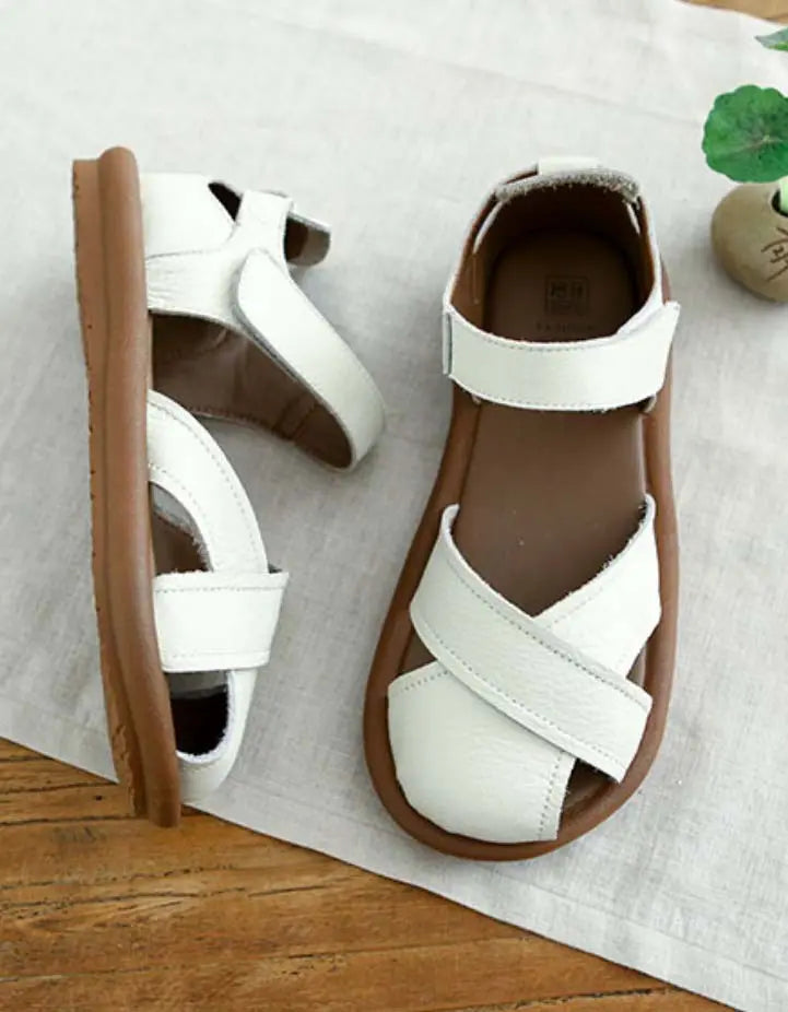 Une paire de sandales plates pour femmes au design moderne, avec des brides croisées en cuir blanc et une semelle en caoutchouc souple de couleur marron. Ces sandales offrent un confort optimal et un style élégant, parfaites pour les journées ensoleillées.