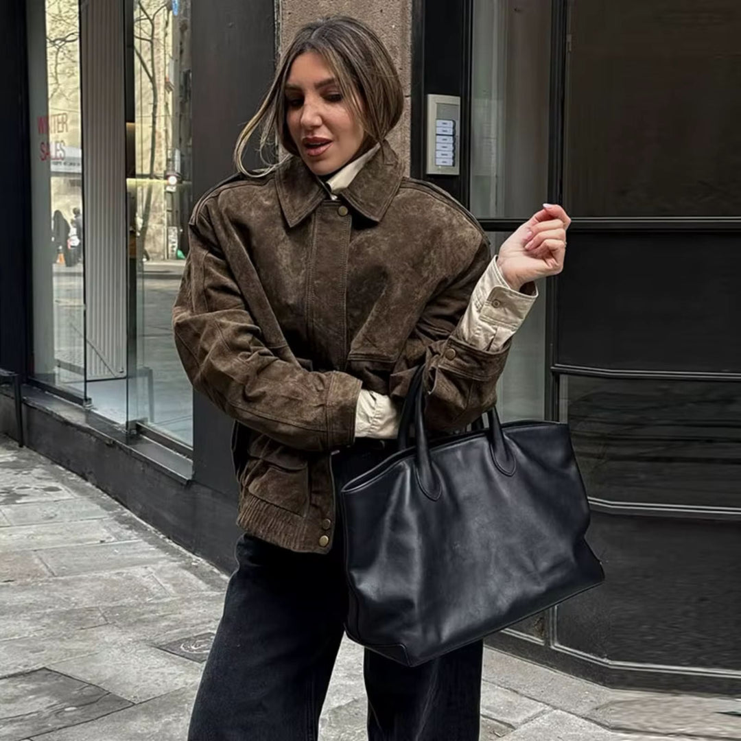 Veste en daim marron au style oversize, associée à un pull beige et un sac à main noir, offrant une tenue élégante et décontractée idéale pour les sorties urbaines.