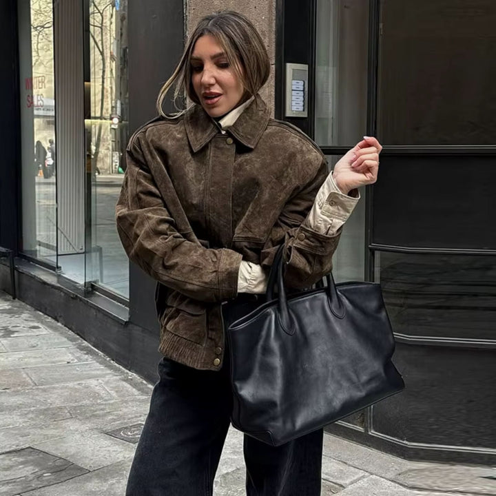 Veste en daim marron au style oversize, associée à un pull beige et un sac à main noir, offrant une tenue élégante et décontractée idéale pour les sorties urbaines.