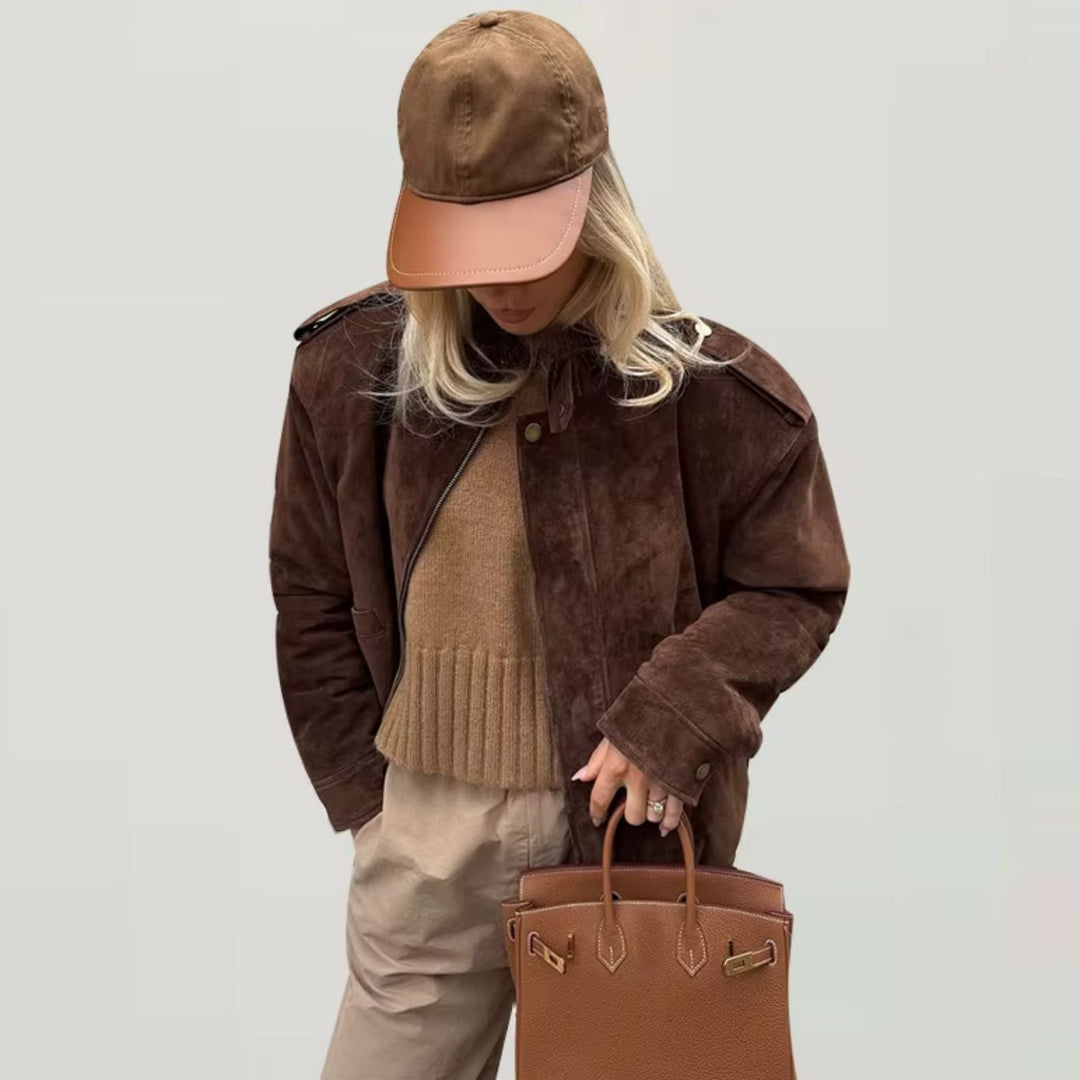 Veste en daim marron au style décontracté, associée à un pull beige et un sac à main élégant, parfaite pour une tenue chic et confortable au quotidien. Complétée par une casquette assortie pour un look tendance.