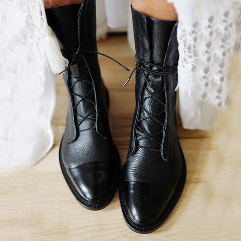 Bottines cheville pour femme en cuir noir avec lacets croisés, bout arrondi et finition élégante, portées avec une tenue claire, au style tendance et chic pour l’automne et l’hiver.