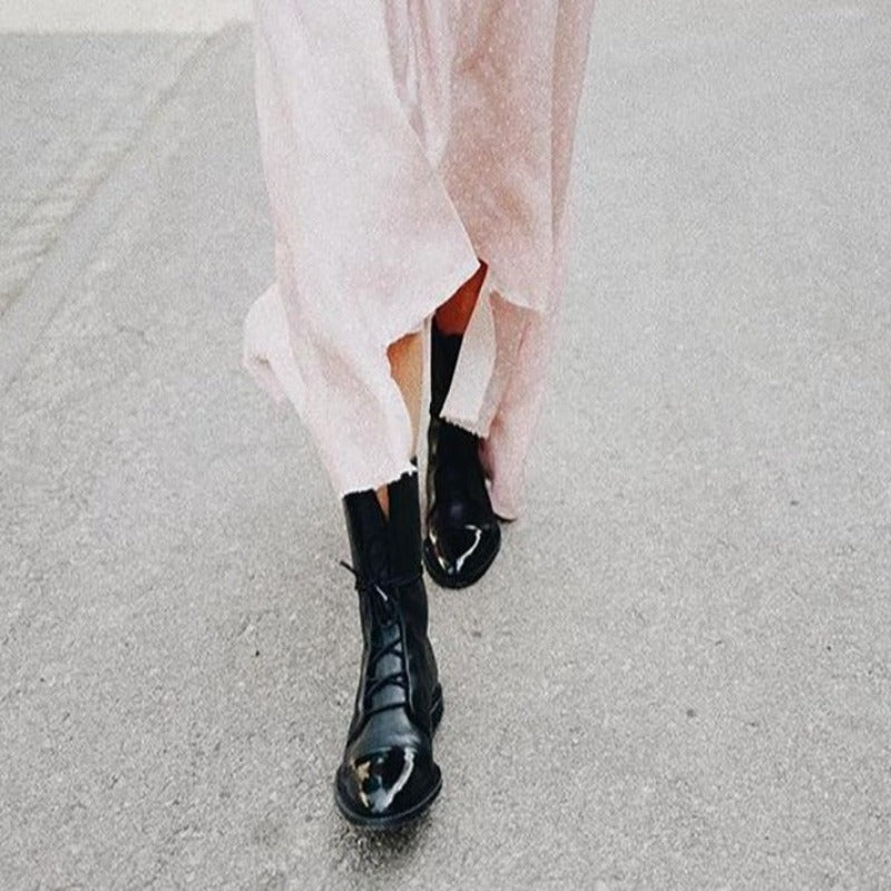 Bottines cheville pour femme en cuir noir avec lacets, semelle robuste et bout arrondi, portées avec une robe longue claire, offrant un style tendance et élégant pour l’automne et l’hiver.