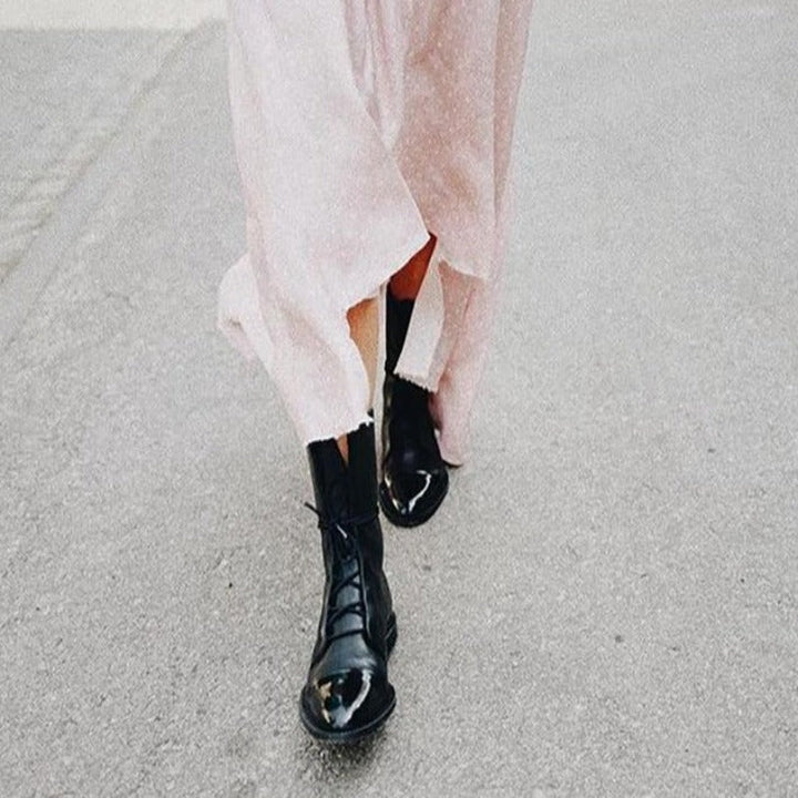Bottines cheville pour femme en cuir noir avec lacets, semelle robuste et bout arrondi, portées avec une robe longue claire, offrant un style tendance et élégant pour l’automne et l’hiver.