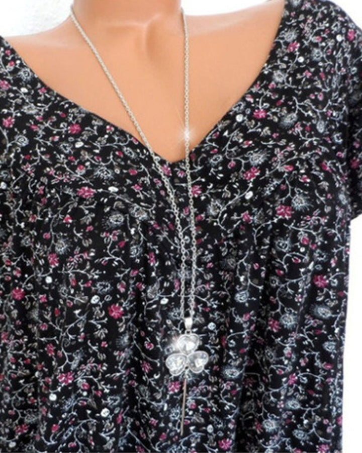 Gros plan de la blouse Verity pour femme, col V et manches courtes, tissu fluide noir à imprimé fleuri moderne petites fleurs roses et motifs blancs, idéale pour un look casual chic.